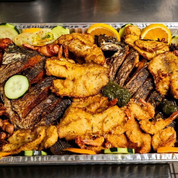 A large foil tray filled with various fried and grilled seafood, garnished with orange slices and cucumber.