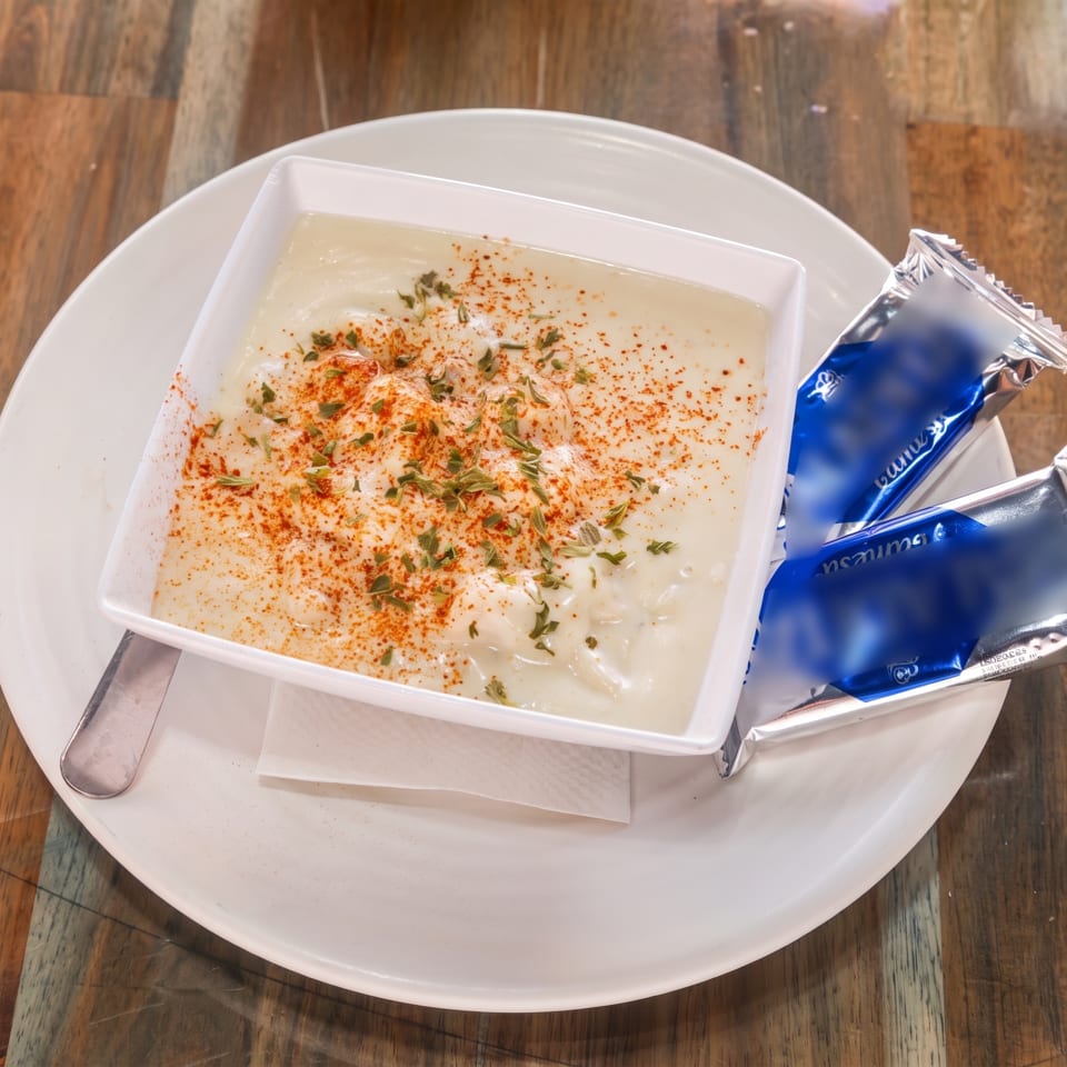 Creamy white soup with red paprika and green herbs, served with two blue packets on a white plate.