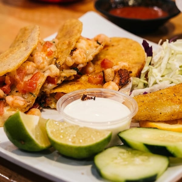 Shrimp tacos with melted cheese, diced tomatoes, shredded cabbage, lime, cucumber, and dipping sauce.