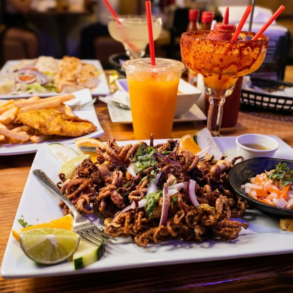 A table laden with plates of fried seafood, including calamari, fish and chips, and drinks.