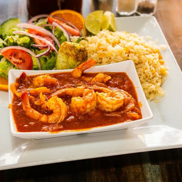 Shrimp in red sauce with rice, salad, and citrus slices on a white plate.