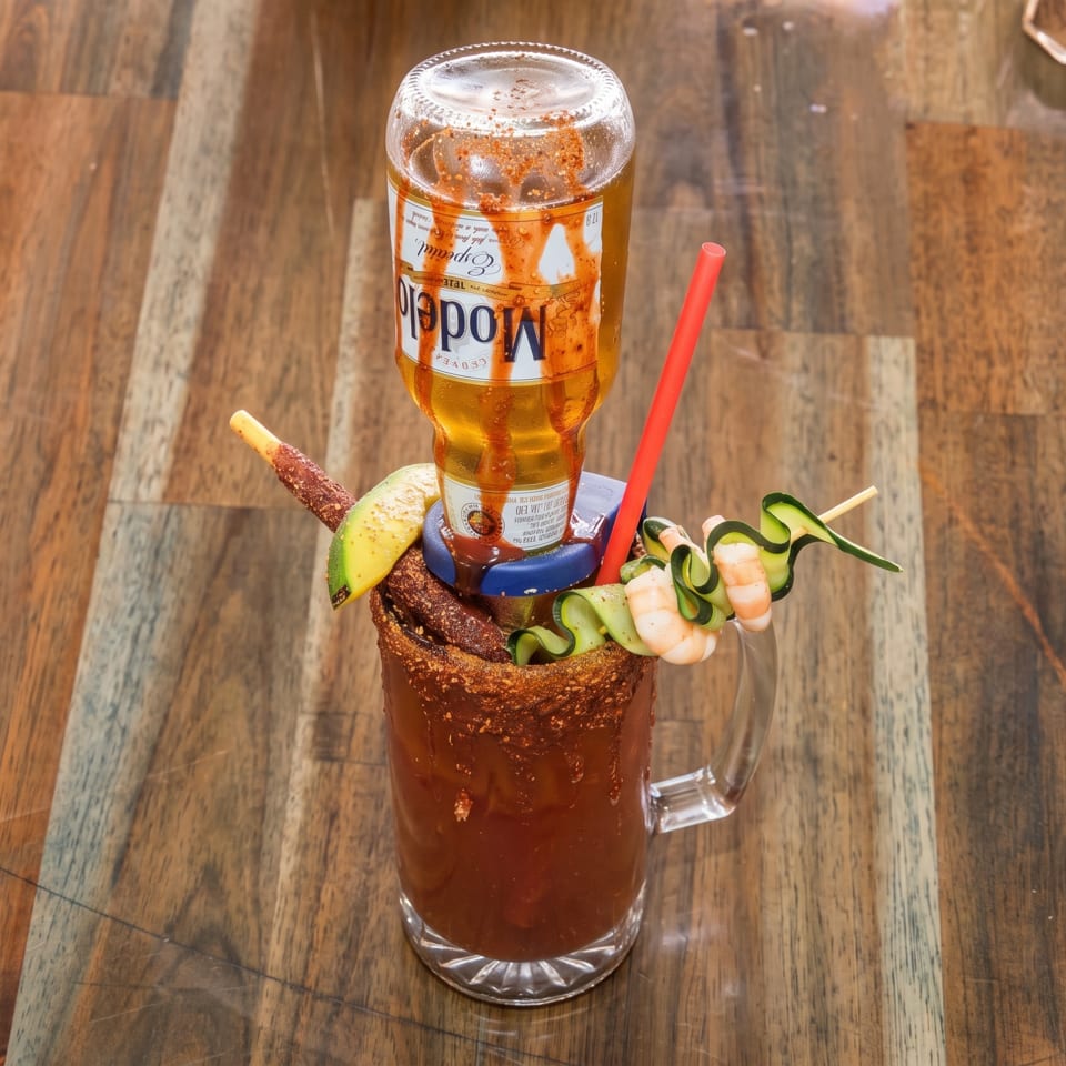 Michelada cocktail with an inverted Modelo beer, shrimp, cucumber, and avocado on a wooden table.