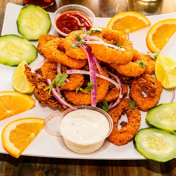 Crispy fried shrimp and calamari rings with cucumber, orange, lime, and dipping sauces on a white plate.