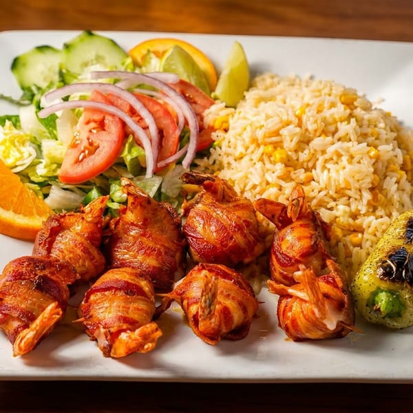 Bacon-wrapped shrimp with rice, salad, orange, lime, and grilled pepper on a white plate.